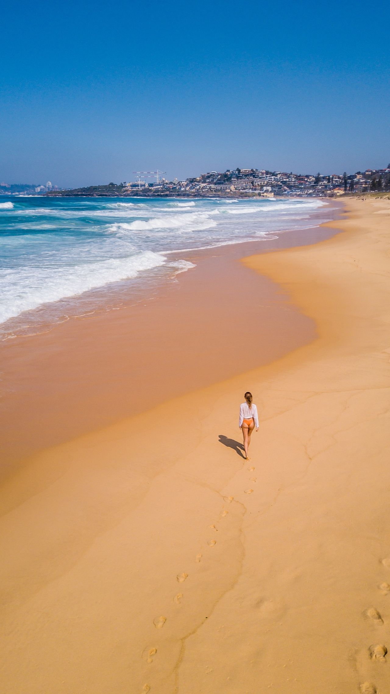A figure walking a golden beach, from directly above