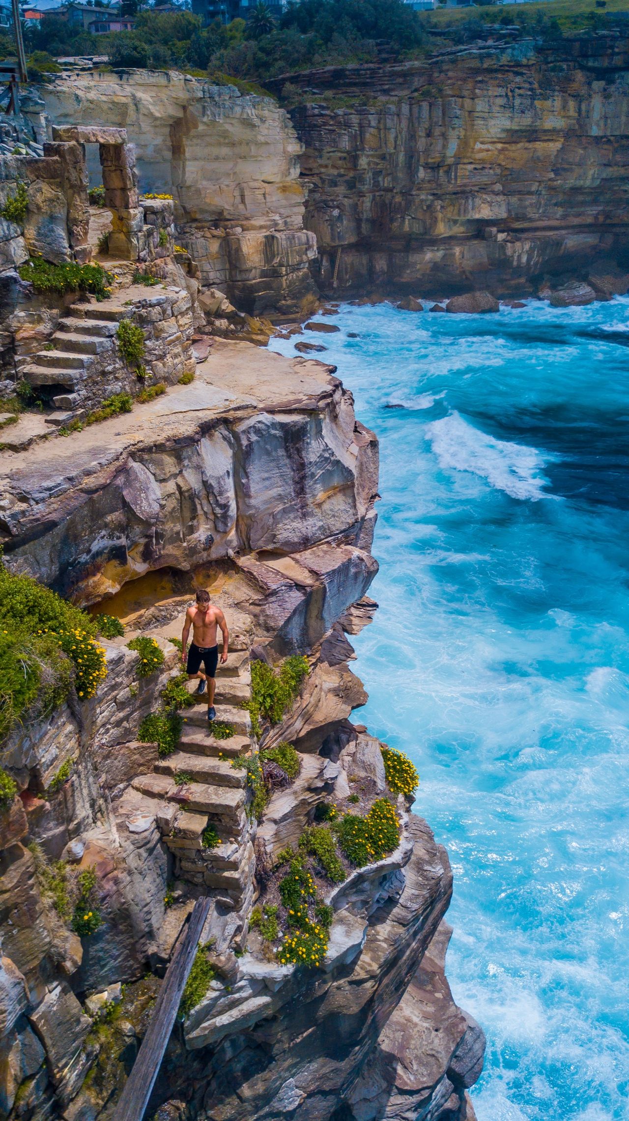 Swimmers below sandstone sea cliffs, from above
