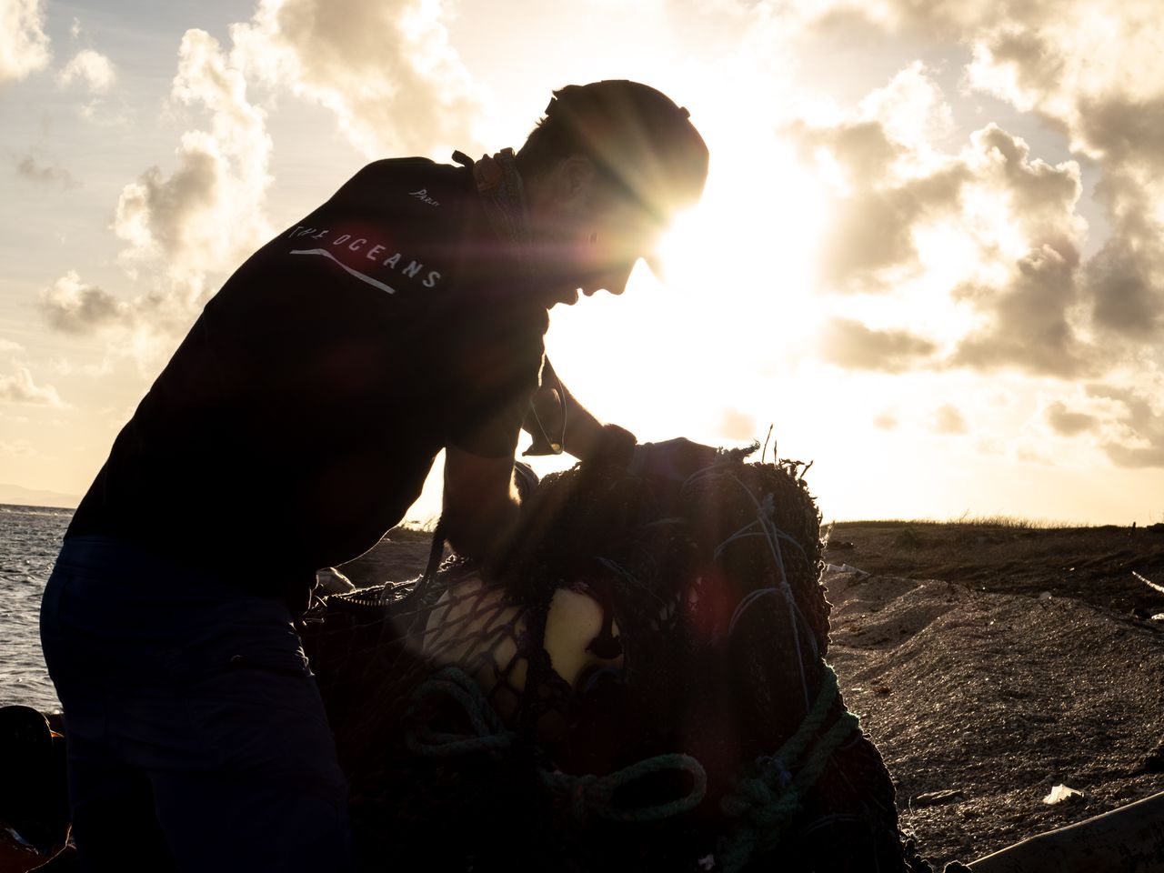 A volunteer hauling a bag of beach plastic, backlit by the sun