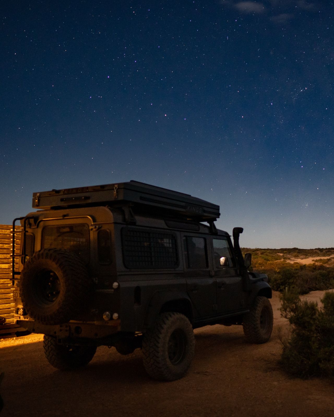 A Land Rover Defender under a night sky full of stars