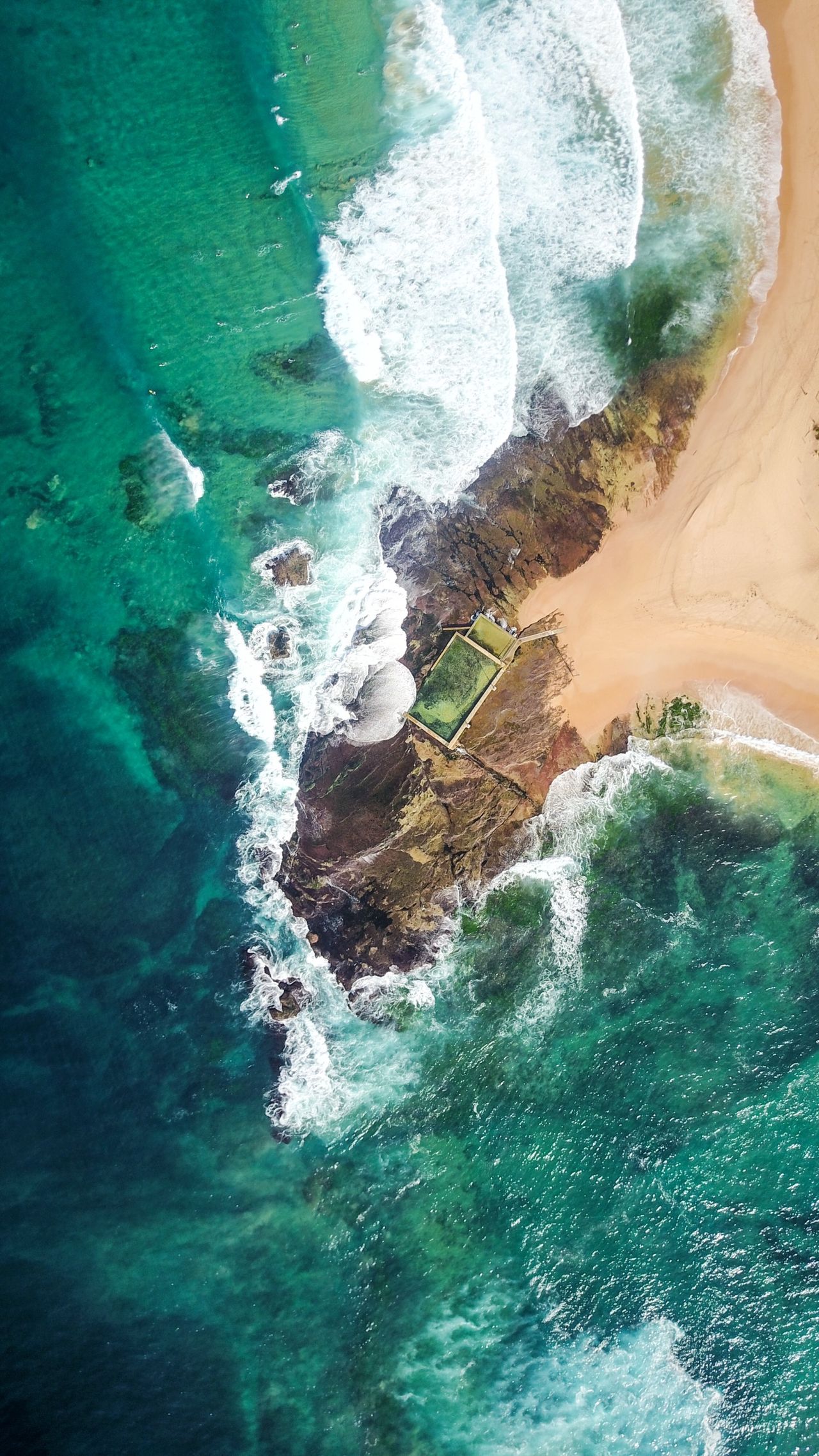 A rocky headland and tidal pool ringed by surf, from above