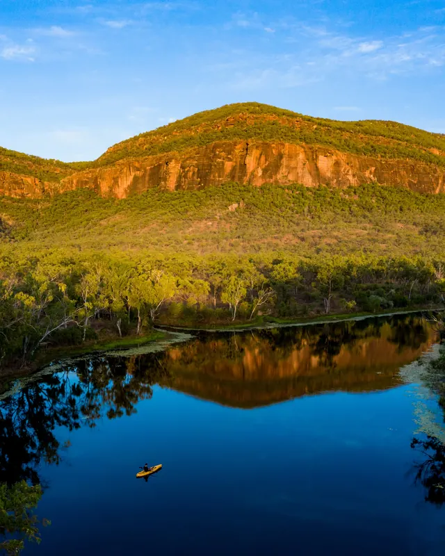 A lone paddler on still water under a sandstone escarpment