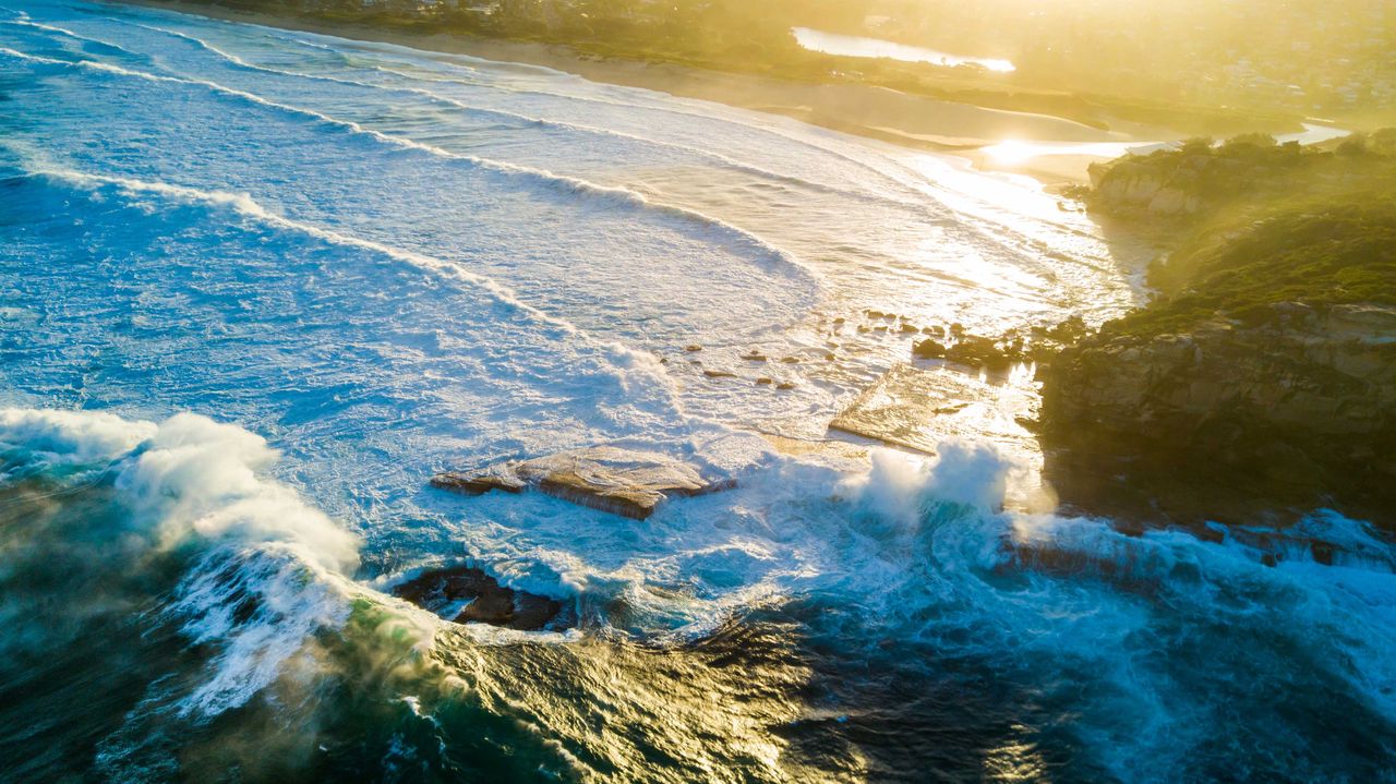 A wave exploding over a rock pool at golden hour