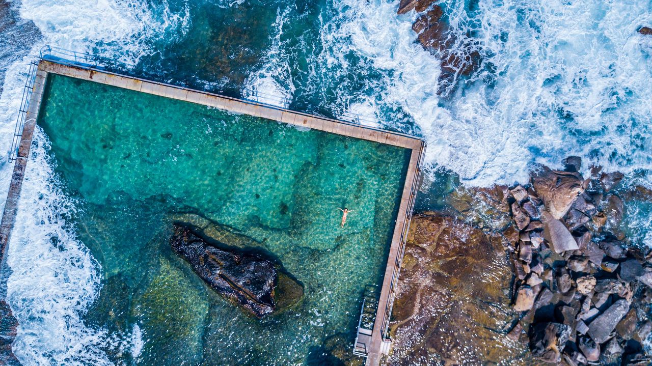 An ocean rock pool with surf breaking around it, from above