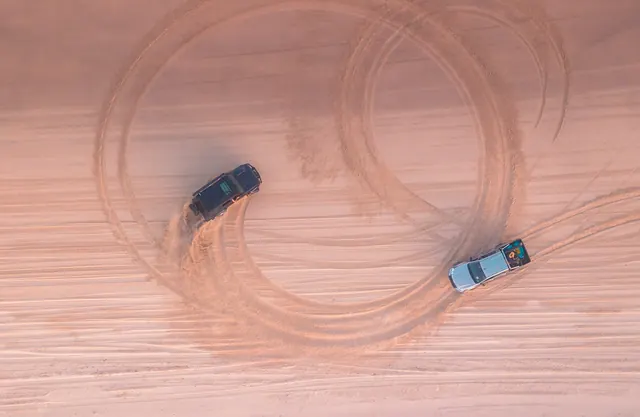 Two cars carving circles in red sand, from above