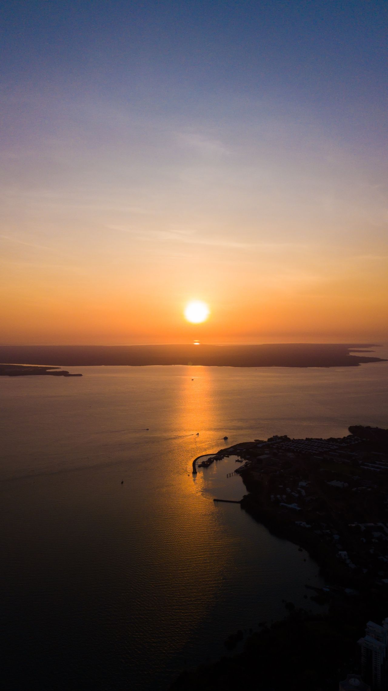 The sun setting into the sea beside a headland