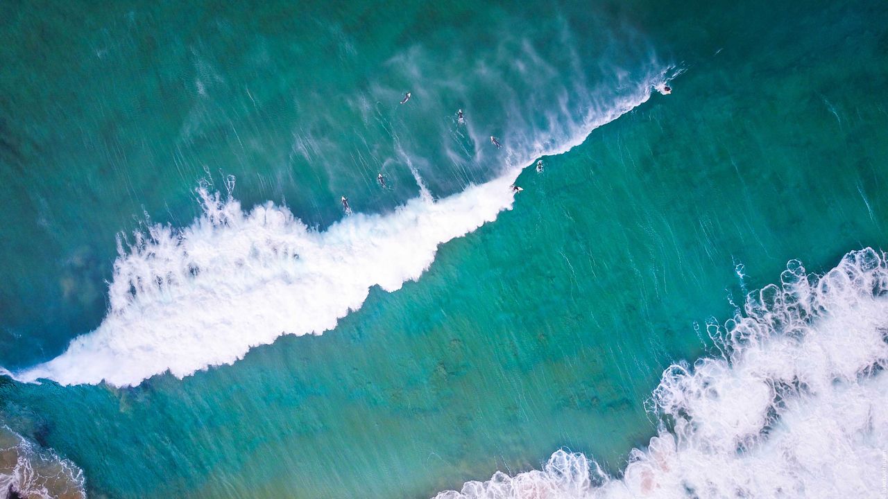 A surfer riding a long green wall of water, from above