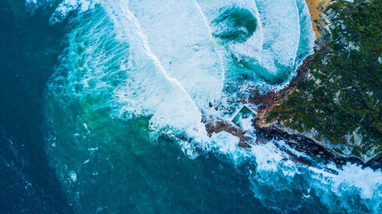Whitewater rolling over a green reef from above