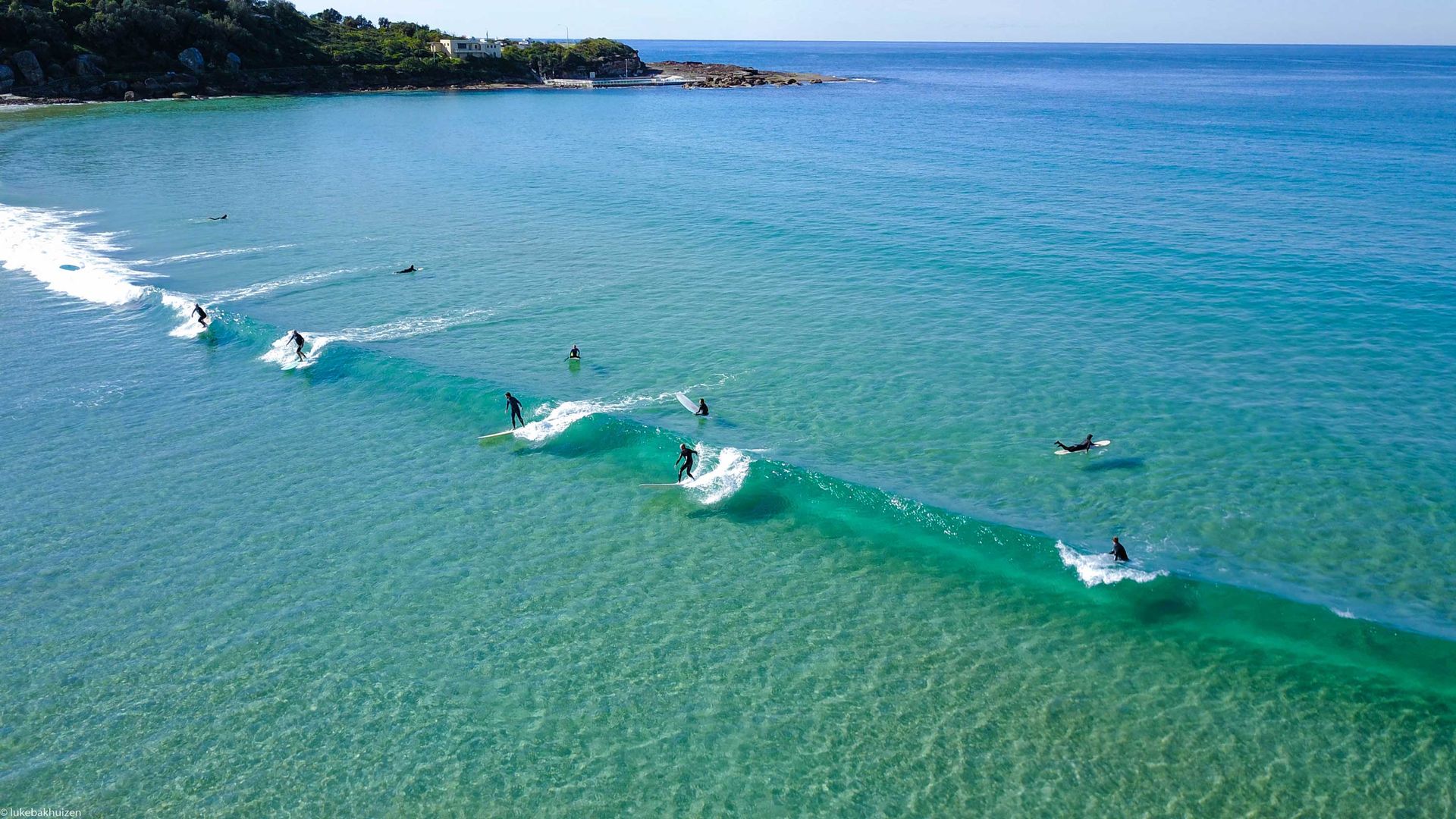 Surfers lined up on a reef break, seen from a drone
